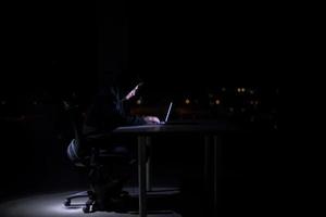 hacker using laptop computer while working in dark office photo