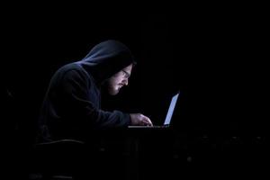 hacker using laptop computer while working in dark office photo