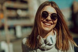 una chica moderna con gafas de sol caminando por la calle escucha música con auriculares. foto