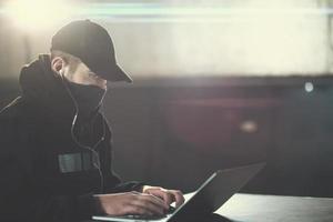 young talented hacker using laptop computer while working in dark office photo