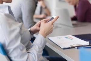 Cerca de las manos de una mujer de negocios usando un teléfono inteligente en una reunión foto