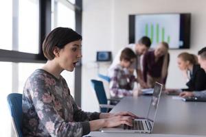 young business woman at office working on laptop with team on meeting in background photo
