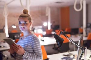 mujer que trabaja en una tableta digital en la oficina nocturna foto