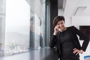 mujer elegante usando teléfono móvil por ventana en edificio de oficinas foto