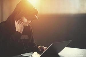 young talented hacker using laptop computer while working in dark office photo