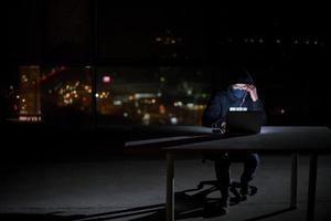 hacker using laptop computer while working in dark office photo