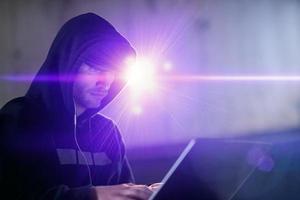 young talented hacker using laptop computer while working in dark office photo