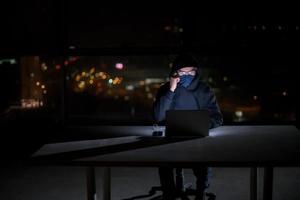 hacker using laptop computer while working in dark office photo