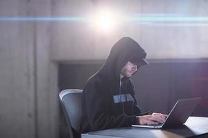 young talented hacker using laptop computer while working in dark office photo