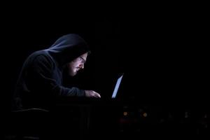 hacker using laptop computer while working in dark office photo