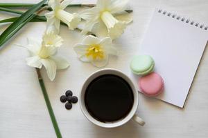 Notepad, macarons, cup of coffee and daffodils on a white table. Inspirational workplace. photo