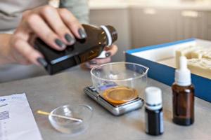 A soap-maker woman weighs aromatic oils for making cosmetics on a kitchen scale. Home spa. Small business photo