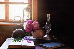 Bodegón de artículos vintage y un ramo de peonías en una mesa junto a la ventana en una antigua casa de pueblo. foto