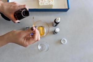 A soap-maker woman weighs aromatic oils for making cosmetics on a kitchen scale. Home spa. Small business photo