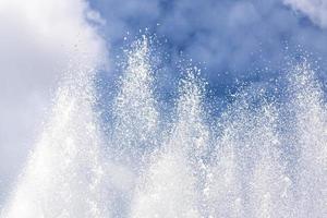 Background of water jets and fountain splashes against a blue sky with clouds photo