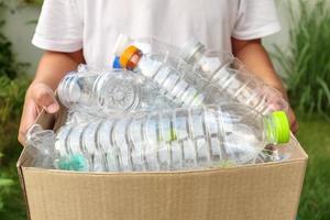 mano que sostiene la caja de basura de reciclaje marrón con botellas de plástico foto