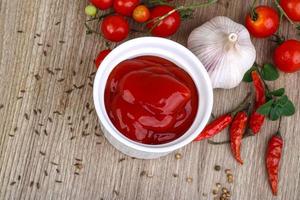 ketchup de tomate en un recipiente sobre fondo de madera foto