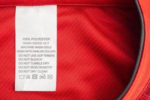 White laundry care washing instructions clothes label on red jersey polyester sport shirt photo