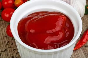 Tomato ketchup in a bowl on wooden background photo