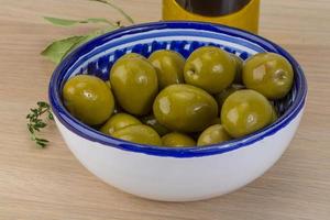 aceitunas verdes en un recipiente sobre fondo de madera foto