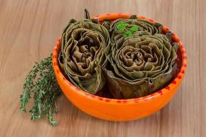 Boiled artichokes in a bowl on wooden background photo