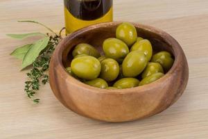 aceitunas verdes en un recipiente sobre fondo de madera foto