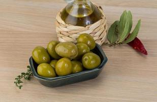 Green olives in a bowl on wooden background photo