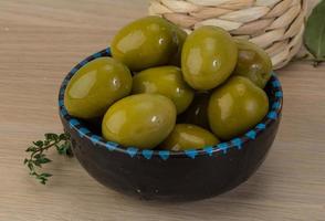 Green olives in a bowl on wooden background photo