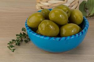 aceitunas verdes en un recipiente sobre fondo de madera foto