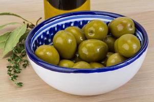 Green olives in a bowl on wooden background photo