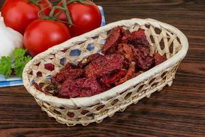 Dried tomtoes in a basket on wooden background photo