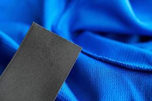 Black blank laundry care clothes label on blue jersey polyester sport shirt background photo