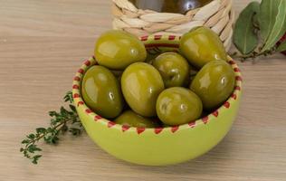 Green olives in a bowl on wooden background photo