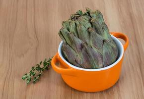 Raw artichokes in a bowl on wooden background photo