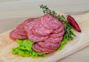 salami en rodajas sobre tablero de madera y fondo de madera foto