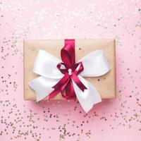 regalo o caja de regalo con un gran lazo en una vista de mesa rosa. composición flatlay para cumpleaños de navidad, día de la madre o boda. foto