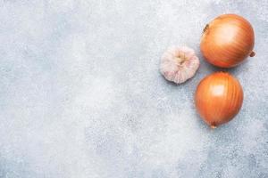 Two raw onions and a head of garlic on a concrete gray background with copy space. photo