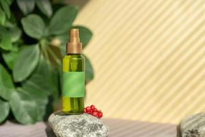 A bottle of green color with a spray bottle lies on the stones, next to the green leaves and berries of schisandra chinensis photo