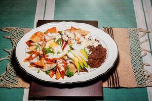 Chilaquiles Mexican food with in red sauce, cheese, cream and chili peppers on vintage background photo