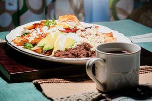 Chilaquiles Mexican food with in red sauce, cheese, cream, chili peppers on vintage background and coffee photo