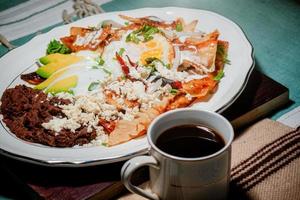 Chilaquiles Mexican food with in red sauce, cheese, cream, chili peppers on vintage background and coffee photo