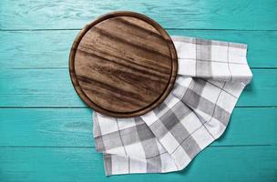 Vintage plaid tablecloth and brown cutting board for pizza on blue wooden table. Wood background. Top view and mock up photo