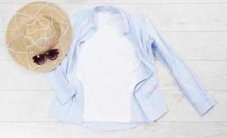 White closeup t shirt mock up flat lay on wooden background. Summer accessories. Hat, sunglasses. Top view and copy space. Mockup t-shirt and summertime. Template blank shirt. photo