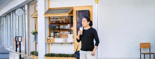 Asian man in the black t-shirt holds the bubble ball ice Milk Tea in front of the shop on the outdoor street footpath. photo