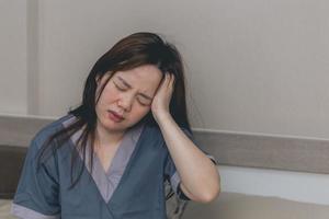 Asian woman are holding their hands to the head in pain on the bed at home, Young women have severe headaches from migraines, Health and illness concept photo