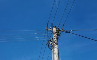 Electric pole power lines outgoing electric wires againts on cloud blue sky. photo