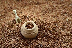 Background image of a large pile of buckwheat, in the middle of which lies a small jug and a wooden spatula for cereals photo