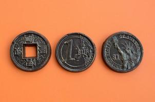 Three chocolate products in the form of Euro, USA and Japan coins lie on an orange plastic background. A model of cash coins in an edible form photo