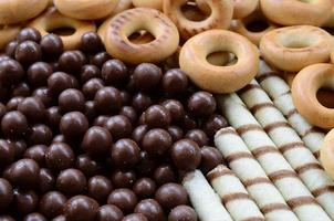 A lot of crispy sweet tubules, chocolate melting balls and yellow bagels lie on a wooden surface. Close up view photo