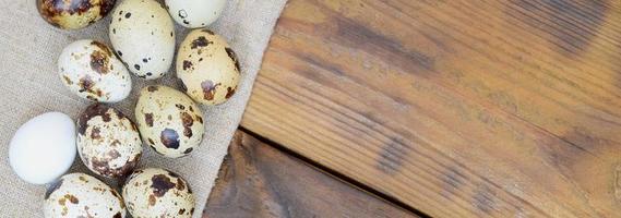 Quail eggs on sacking on a dark brown wooden surface, top view, empty place for text, recipe photo